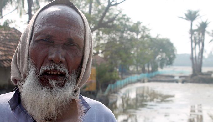 In a village on the edge of the Sundarbans and facing the Bay of Bengal, Jasimuddin Sarkar in front of his farm that now grows nothing, thanks to sea level rise, and his house that gets flooded with dirty saline water every third or fourth day (Photo by Joydeep Gupta)